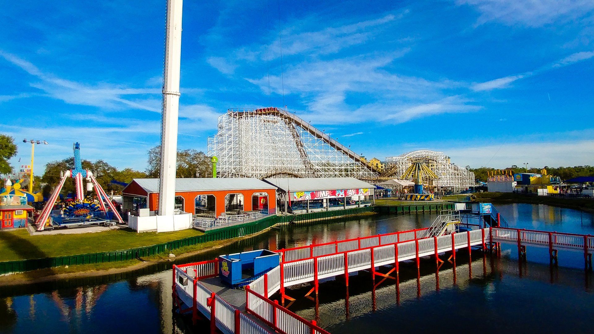 An amusement park with a roller coaster and a bridge over a body of water.