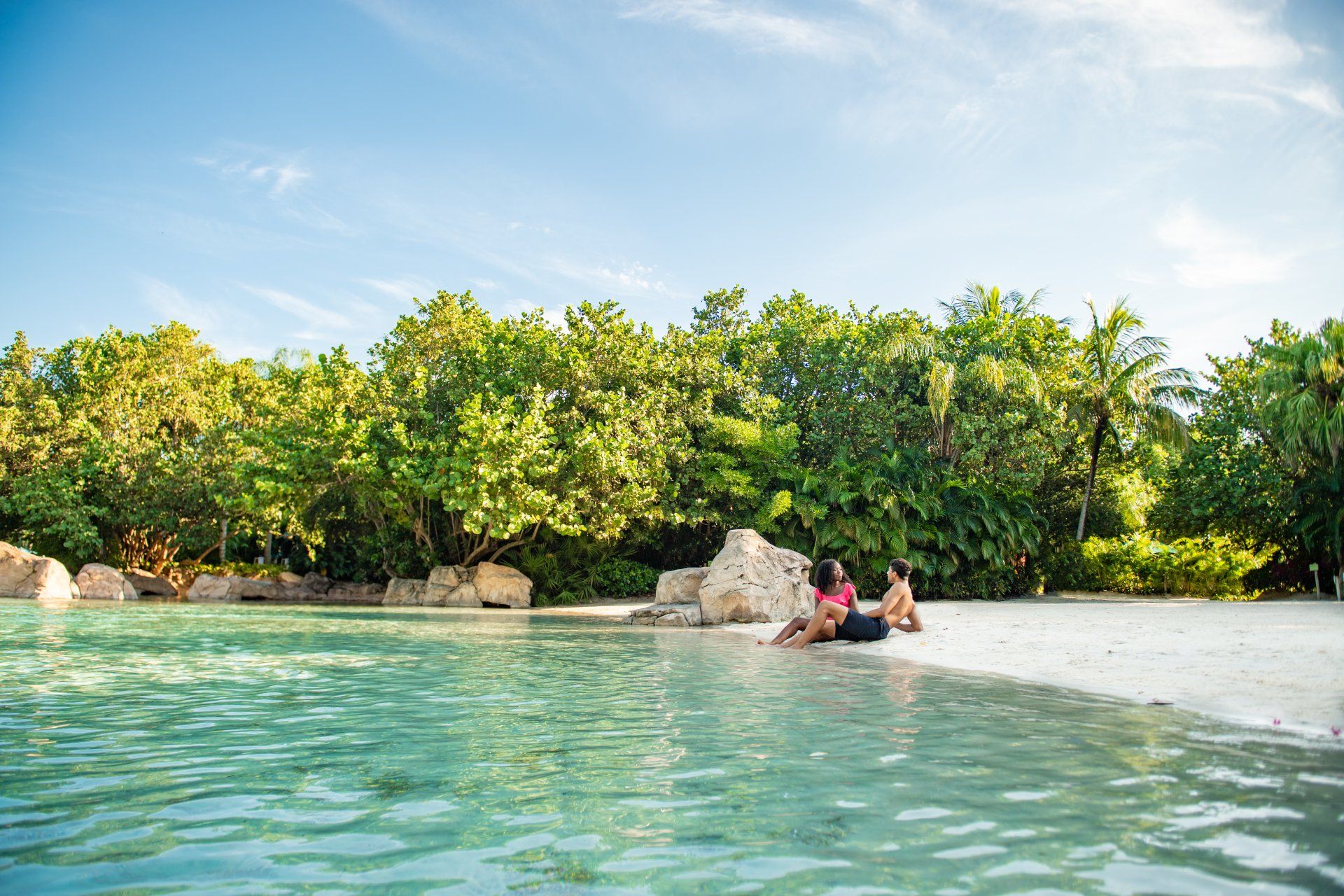 A couple is sitting on a sandy beach next to a body of water.