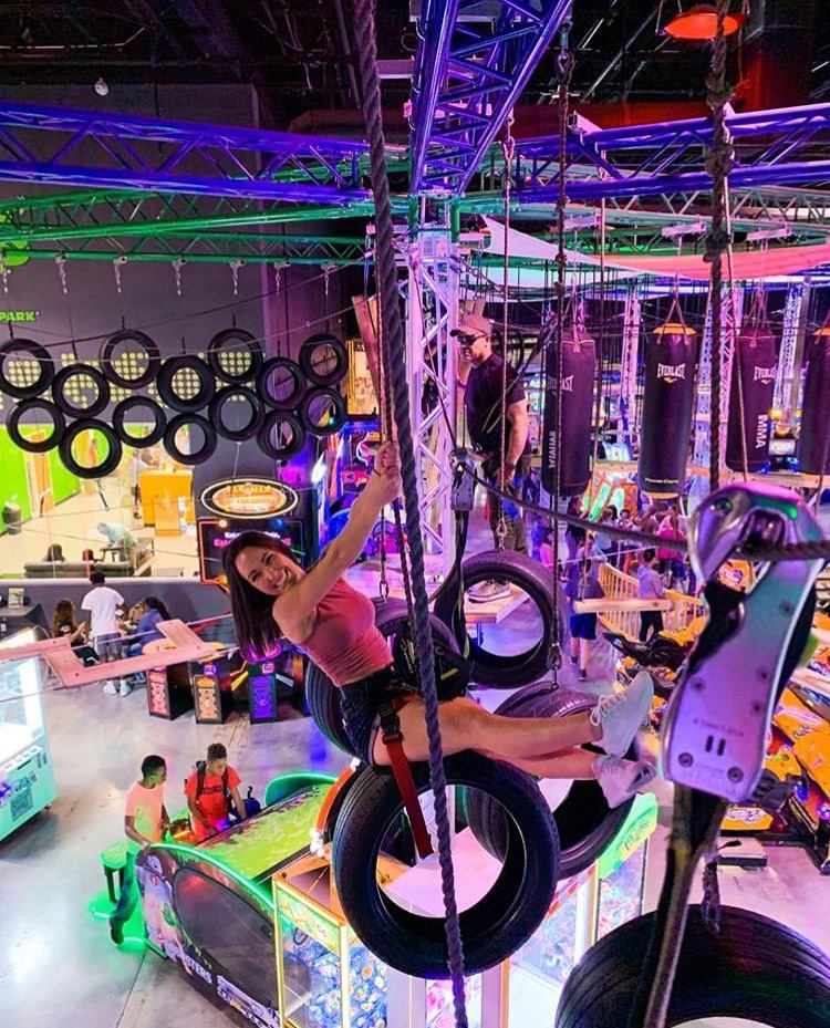 A woman is sitting on a tire swing in an indoor amusement park.