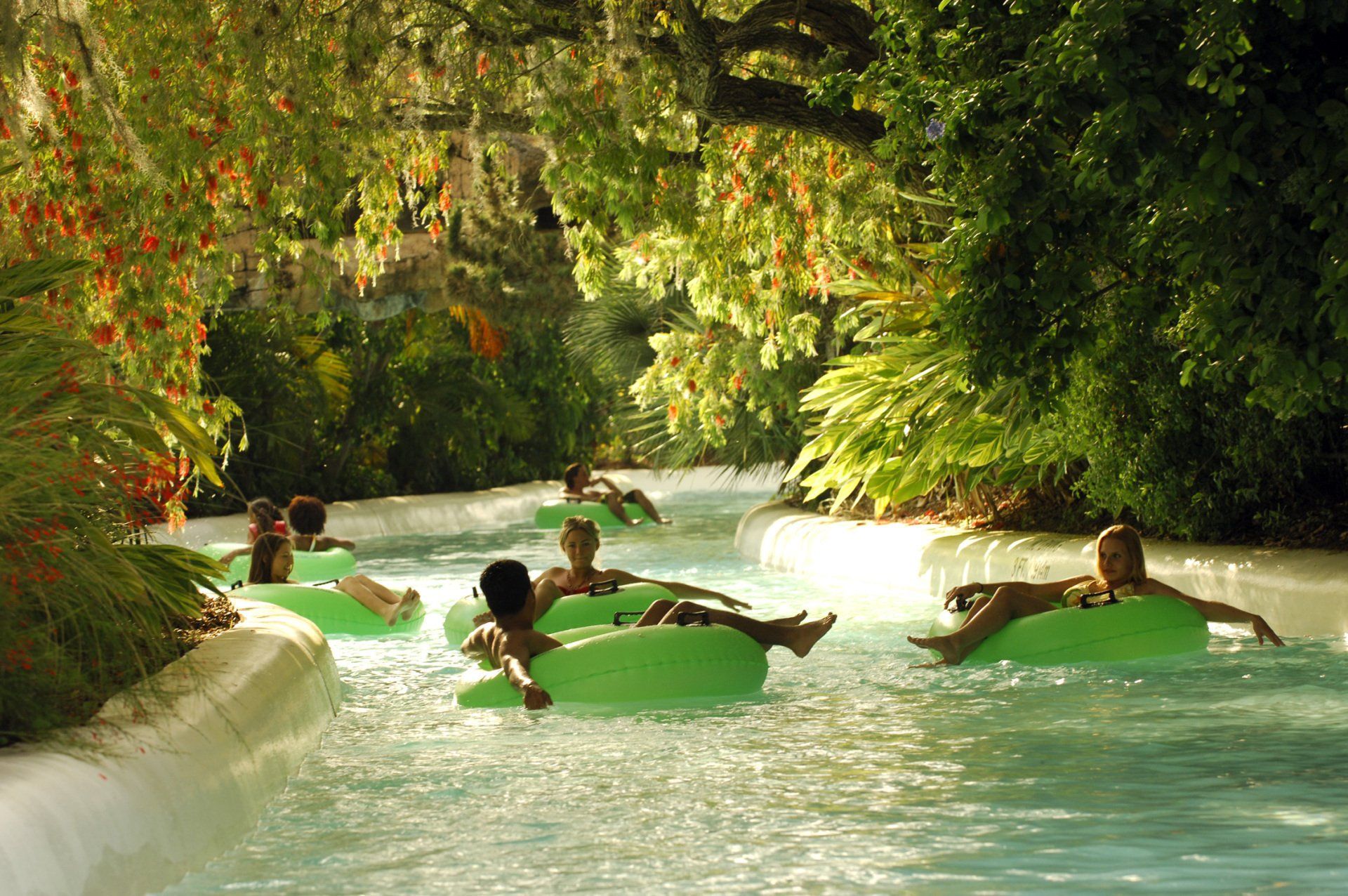 A group of people are floating down a river on green tubes.