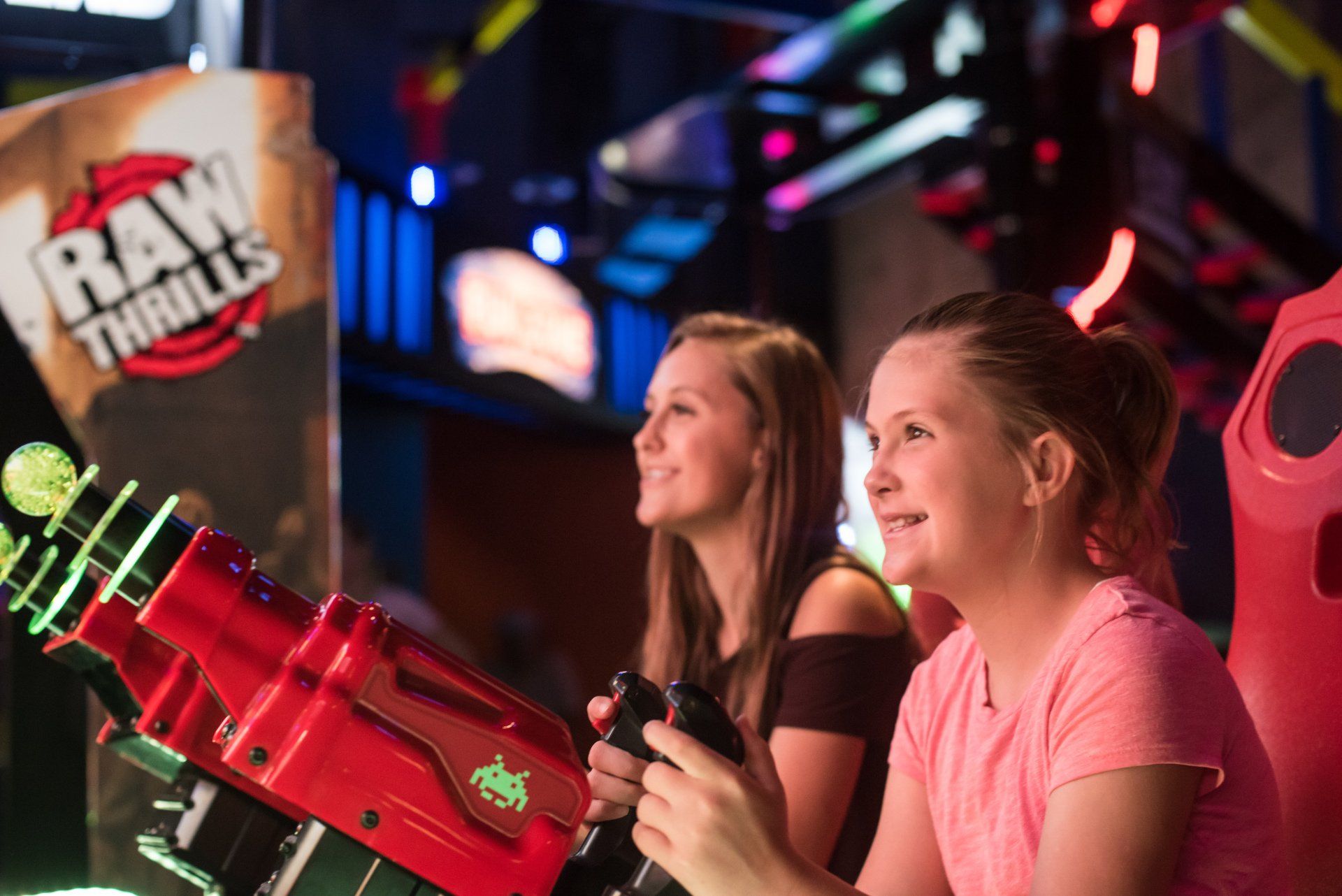Two young girls are playing a video game in an arcade.