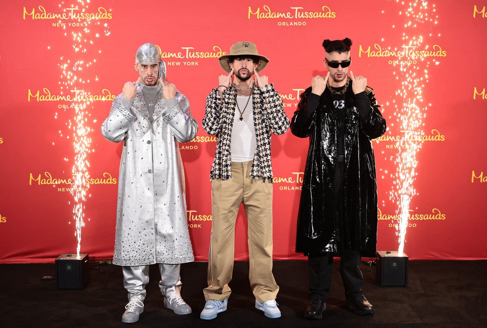 Three men are standing in front of a red wall that says madame tussauds