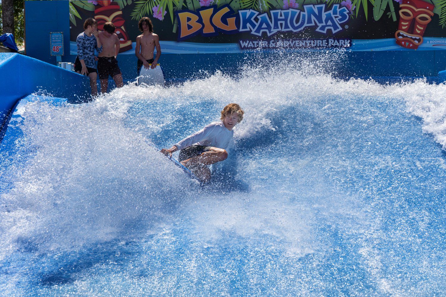 A person is riding a wave in front of a sign that says big kahuna