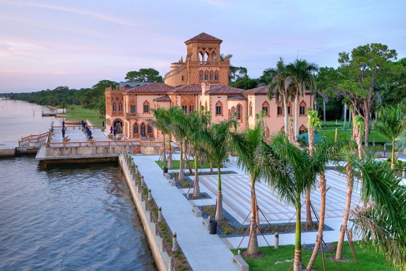A large building is sitting next to a body of water surrounded by palm trees.