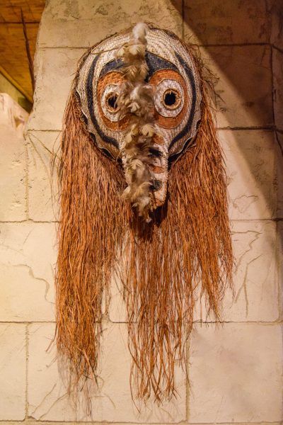 A native american mask with long hair is hanging on a wall.