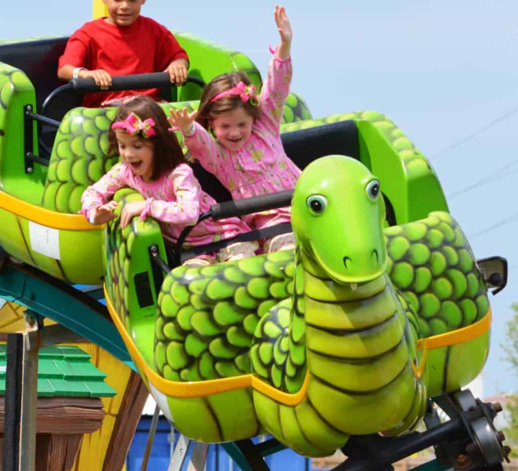 Two little girls are riding a green snake roller coaster