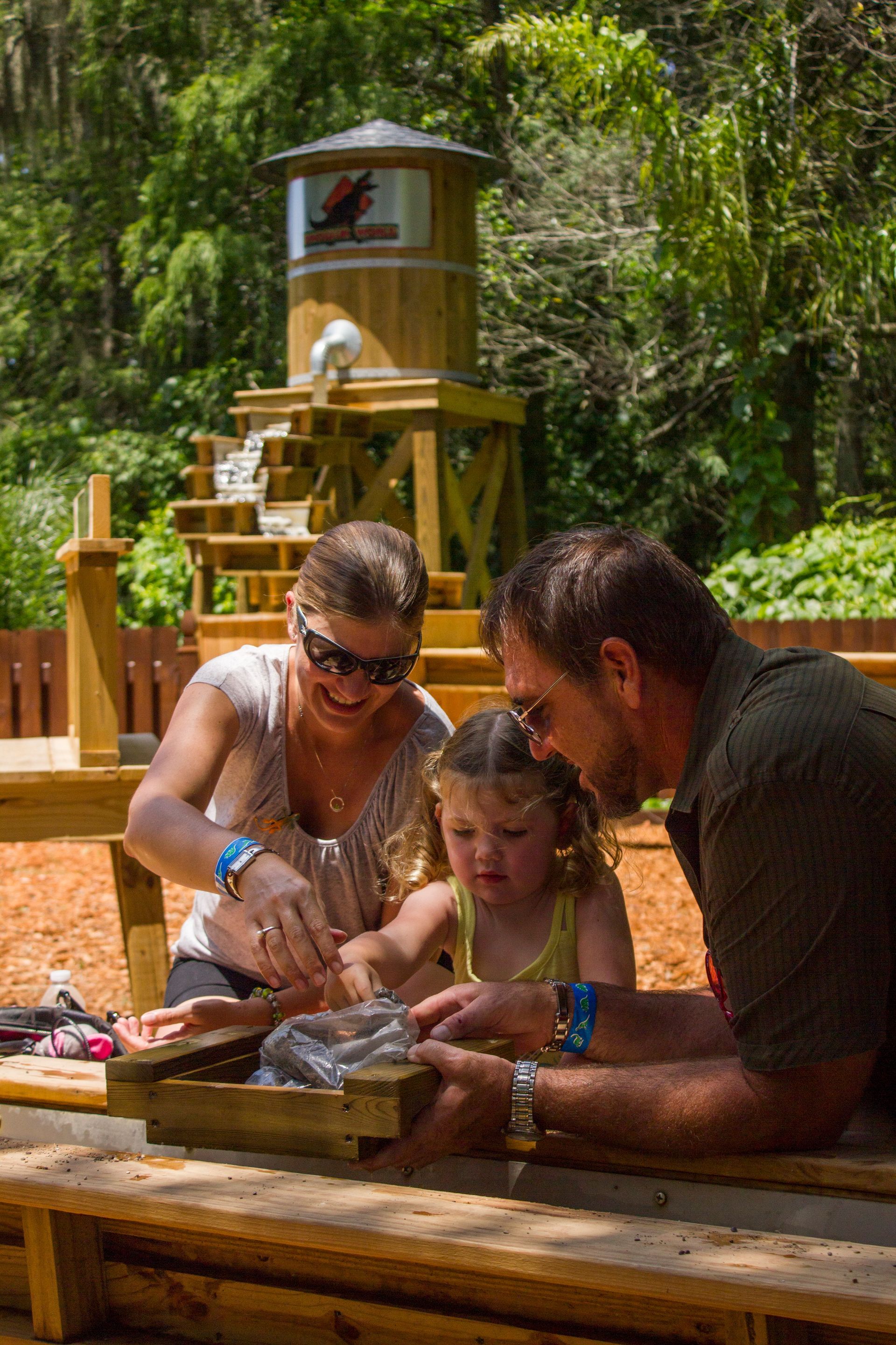 A man and woman are playing with a little girl in a sandbox.