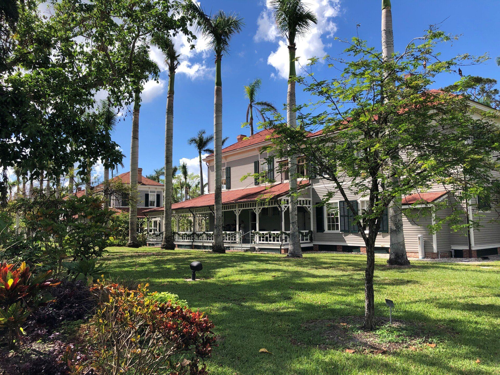 A large white house with a red roof is surrounded by palm trees.