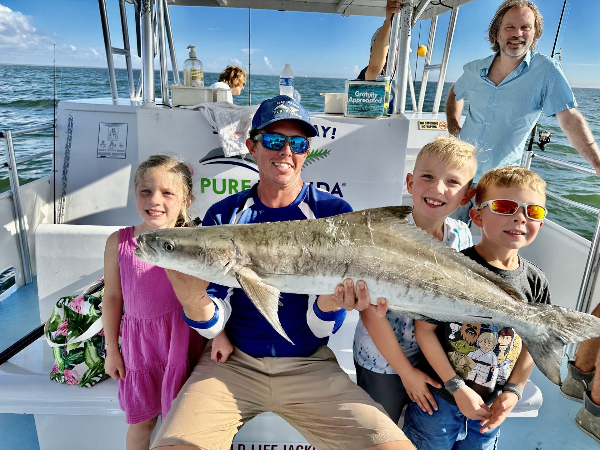 A group of people are sitting on a boat holding a large fish.