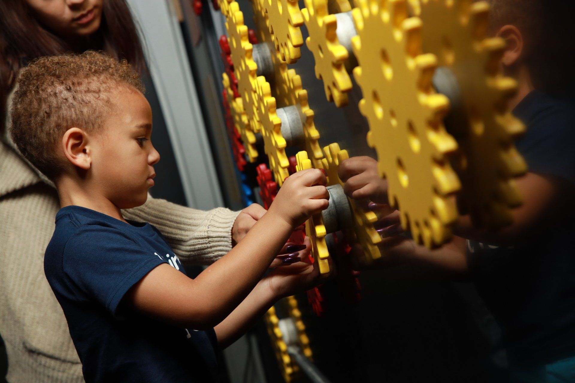 A little boy is playing with a wall of gears