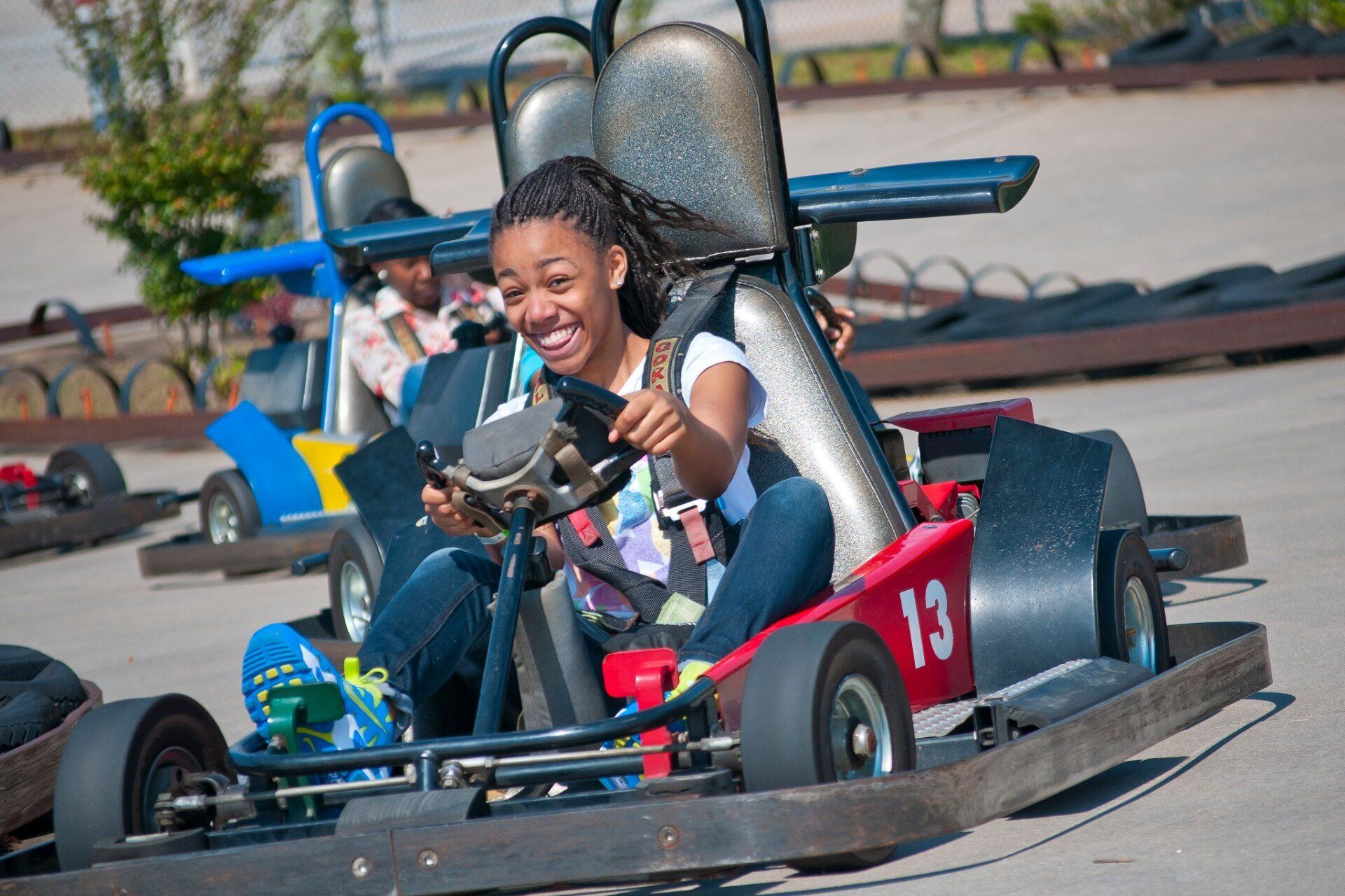 A girl is riding a go kart with the number 13 on the front.
