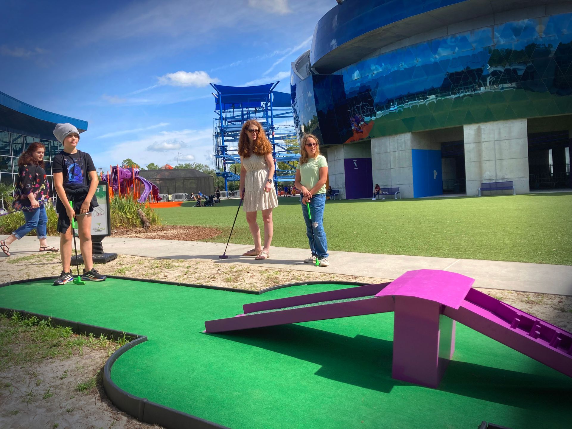A group of children are playing mini golf in front of a building.