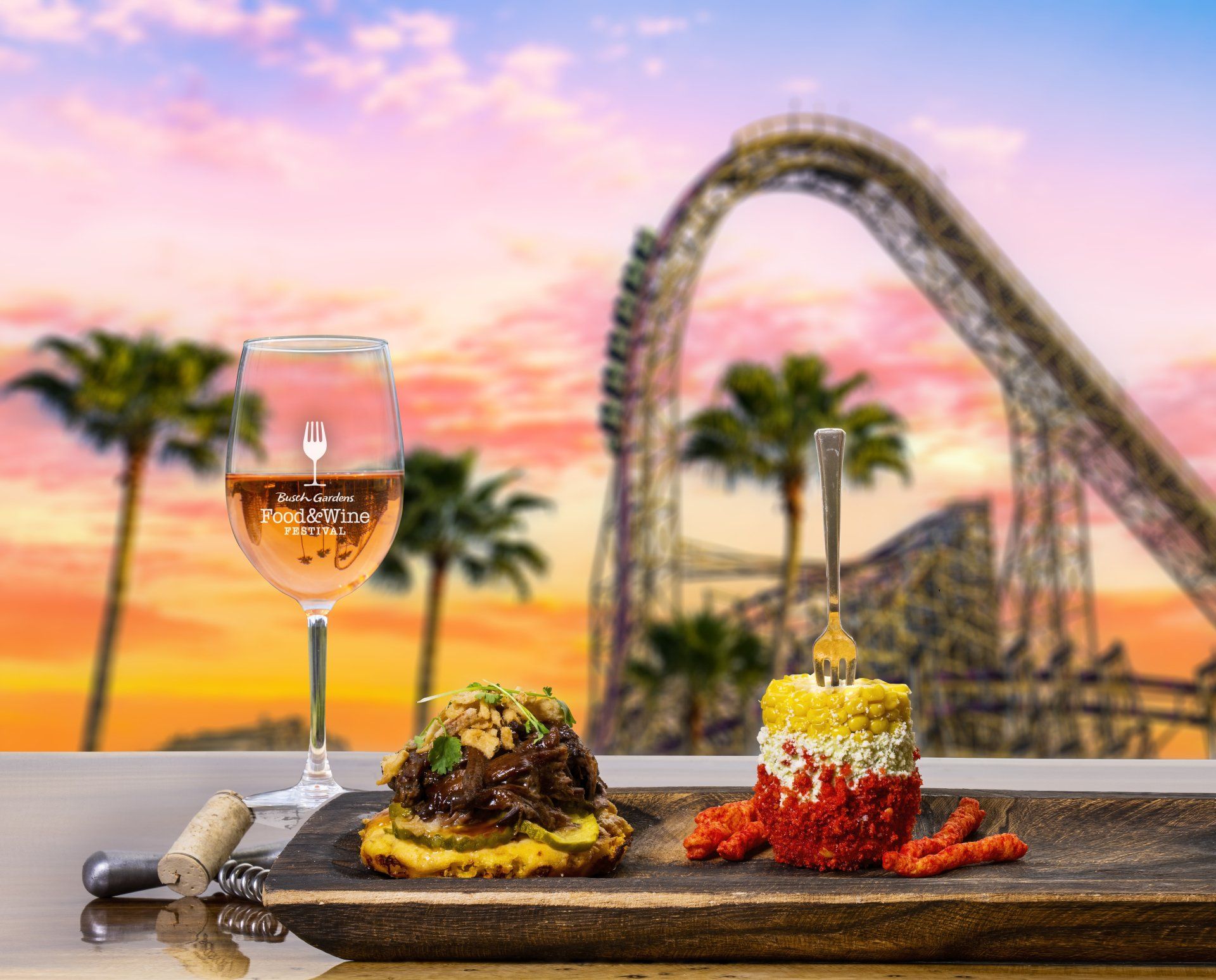 A plate of food and a glass of wine with a roller coaster in the background.