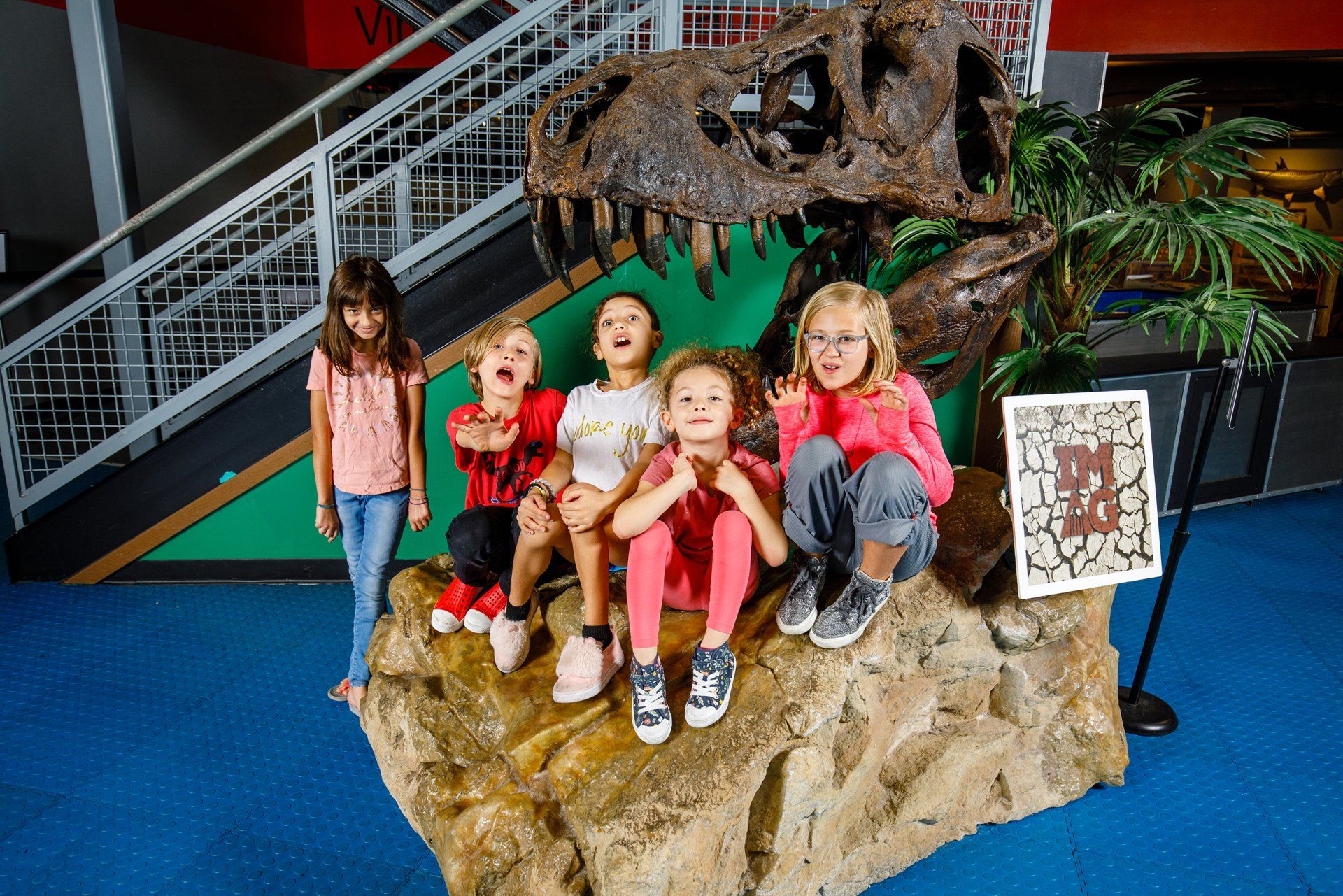 A group of children are posing for a picture in front of a dinosaur skeleton.