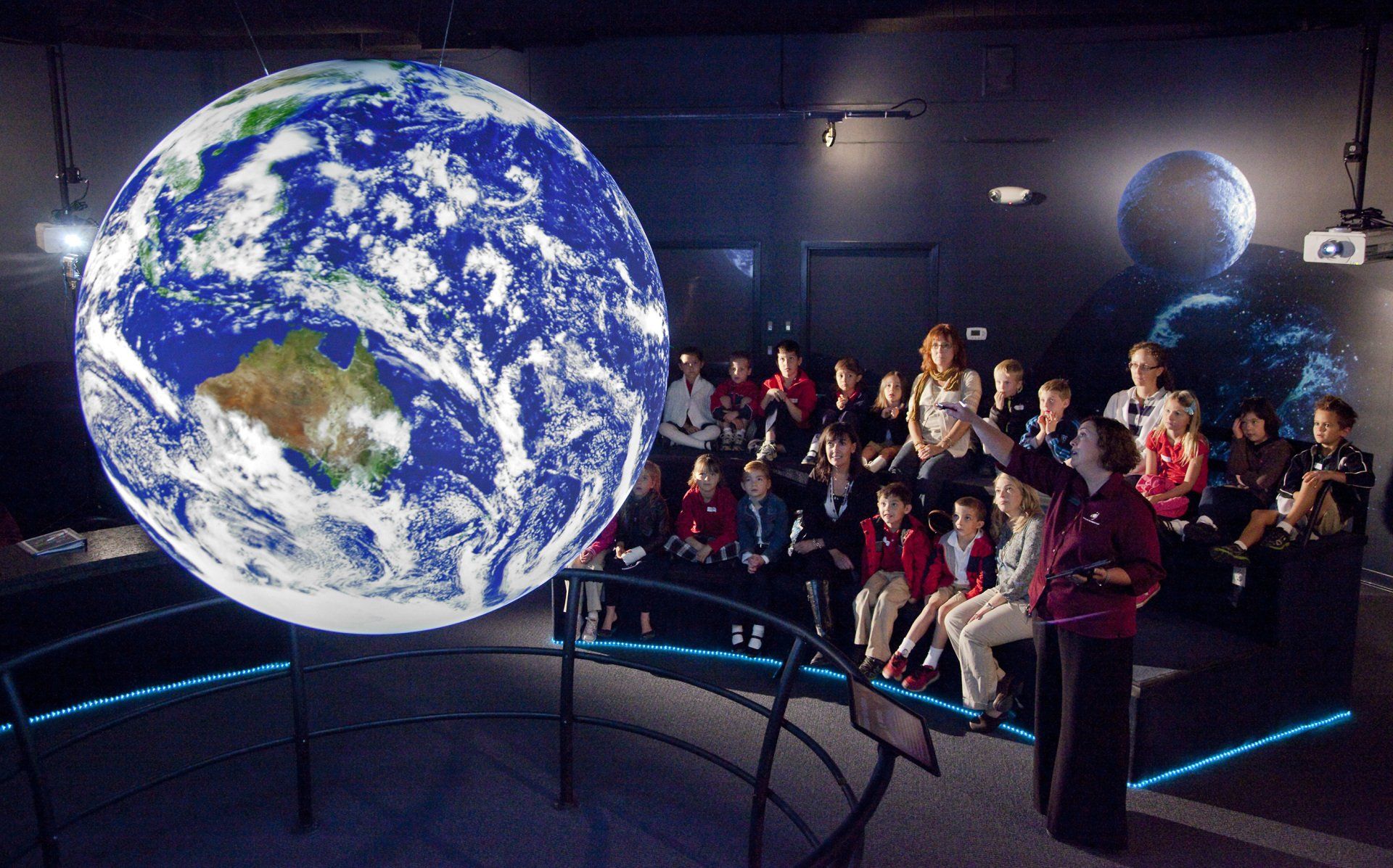 A group of people are sitting in front of a large globe of the earth.
