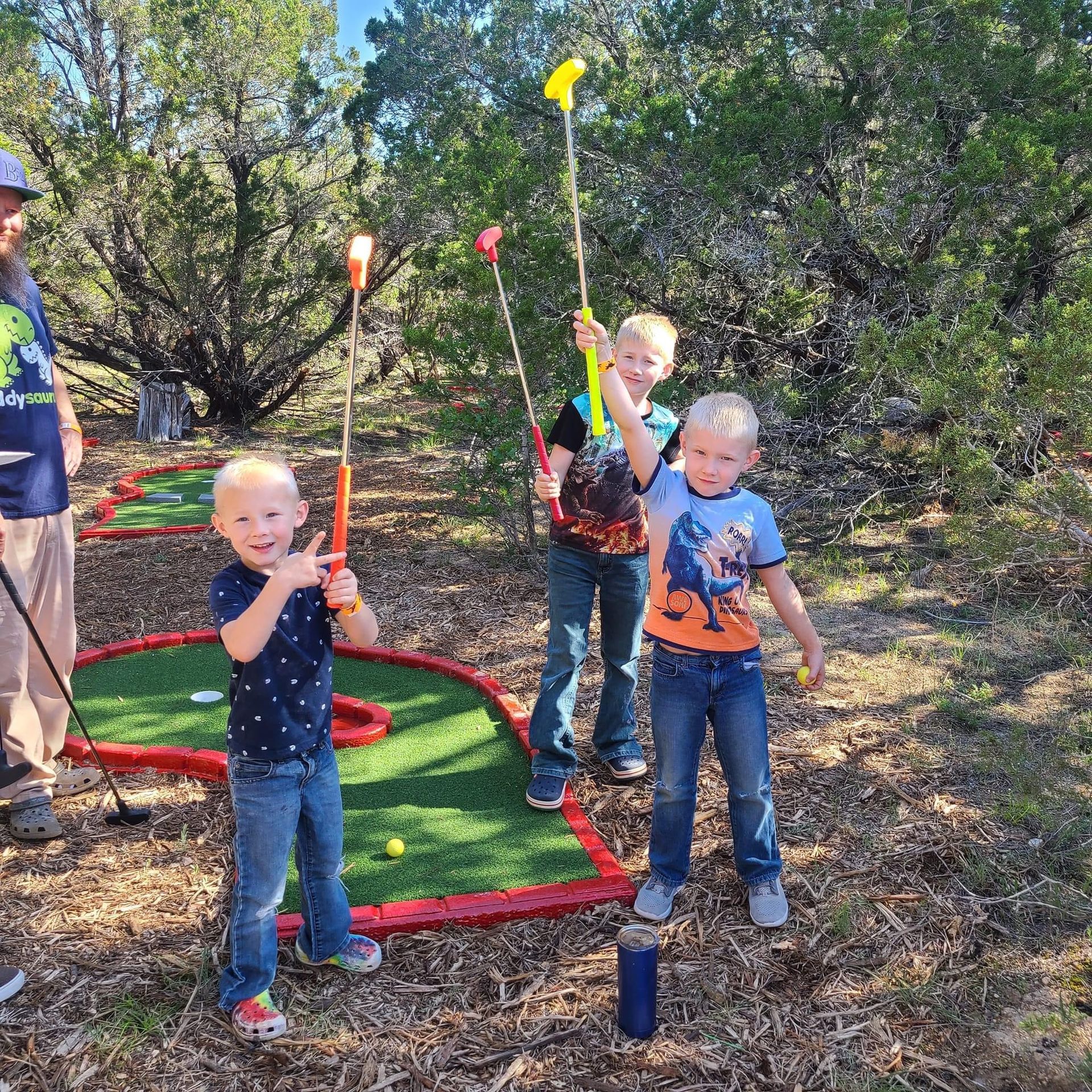Three young boys are playing mini golf in the woods.