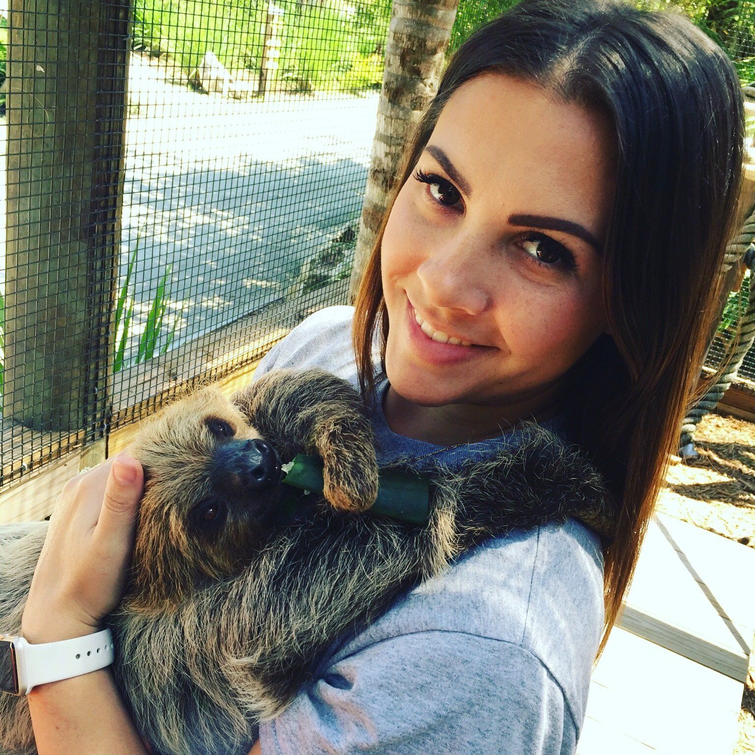 A woman is holding a sloth in her arms and smiling
