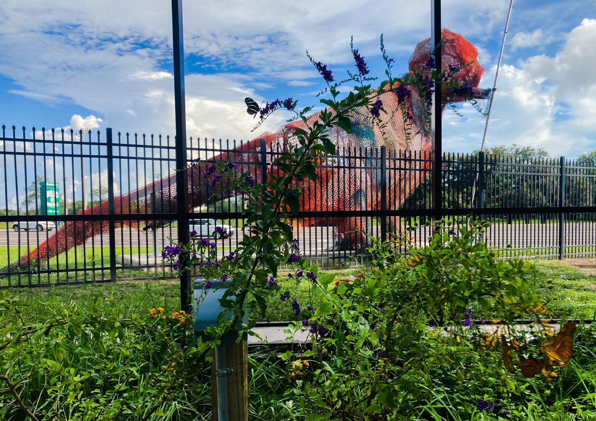 A statue of a dinosaur is behind a fence in a garden.