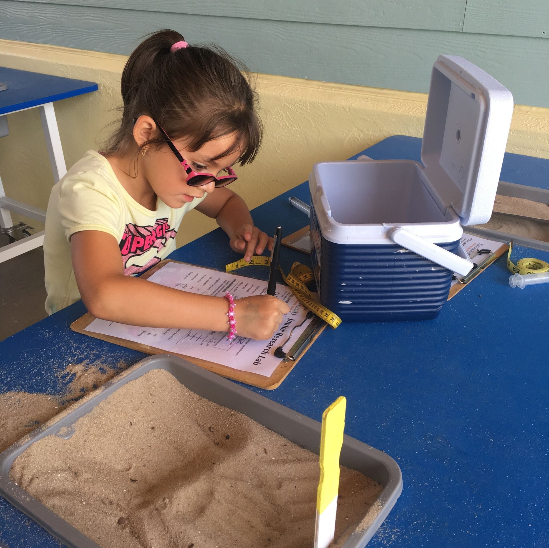 A little girl is sitting at a table writing on a clipboard
