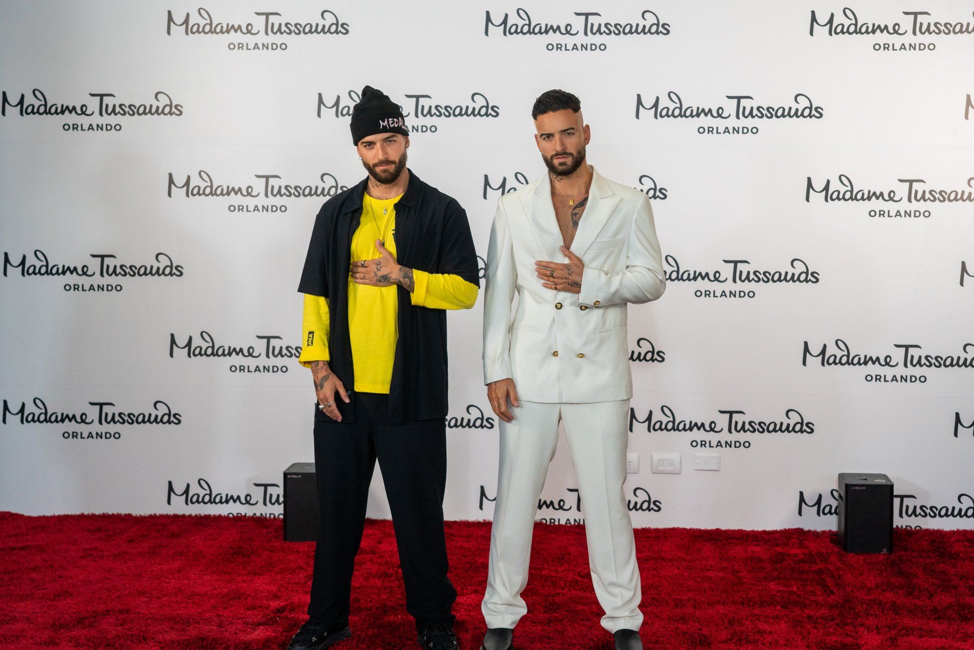 Two men are standing next to each other on a red carpet in front of a wall that says madame tussauds