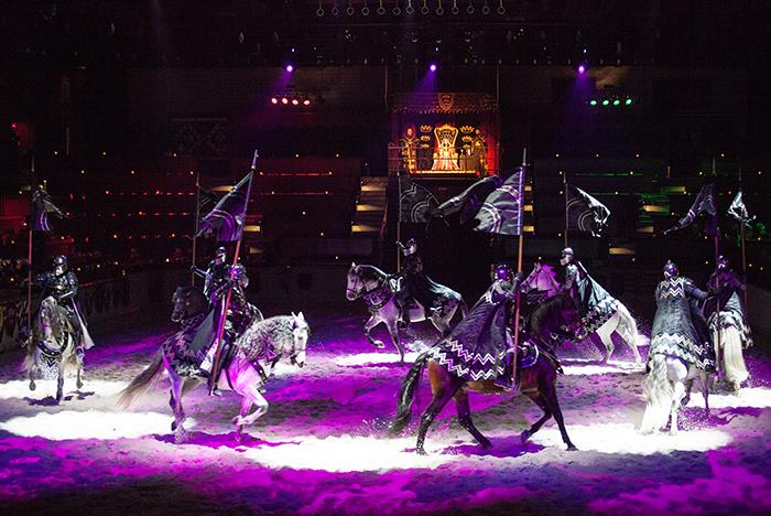A group of knights riding horses on a stage with purple lights.