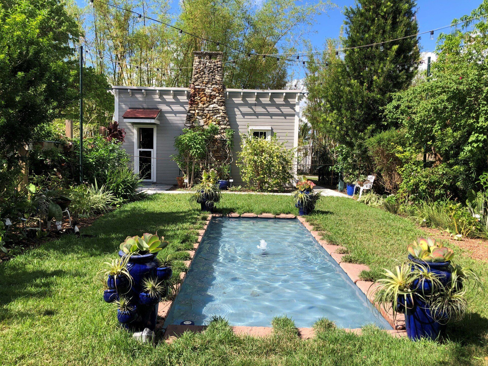There is a small house in the background and a large pool in the middle of the yard.