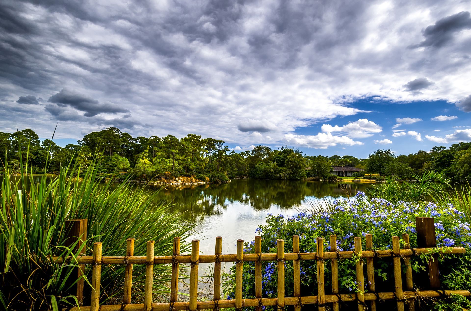 A wooden fence surrounds a lake with flowers in the foreground