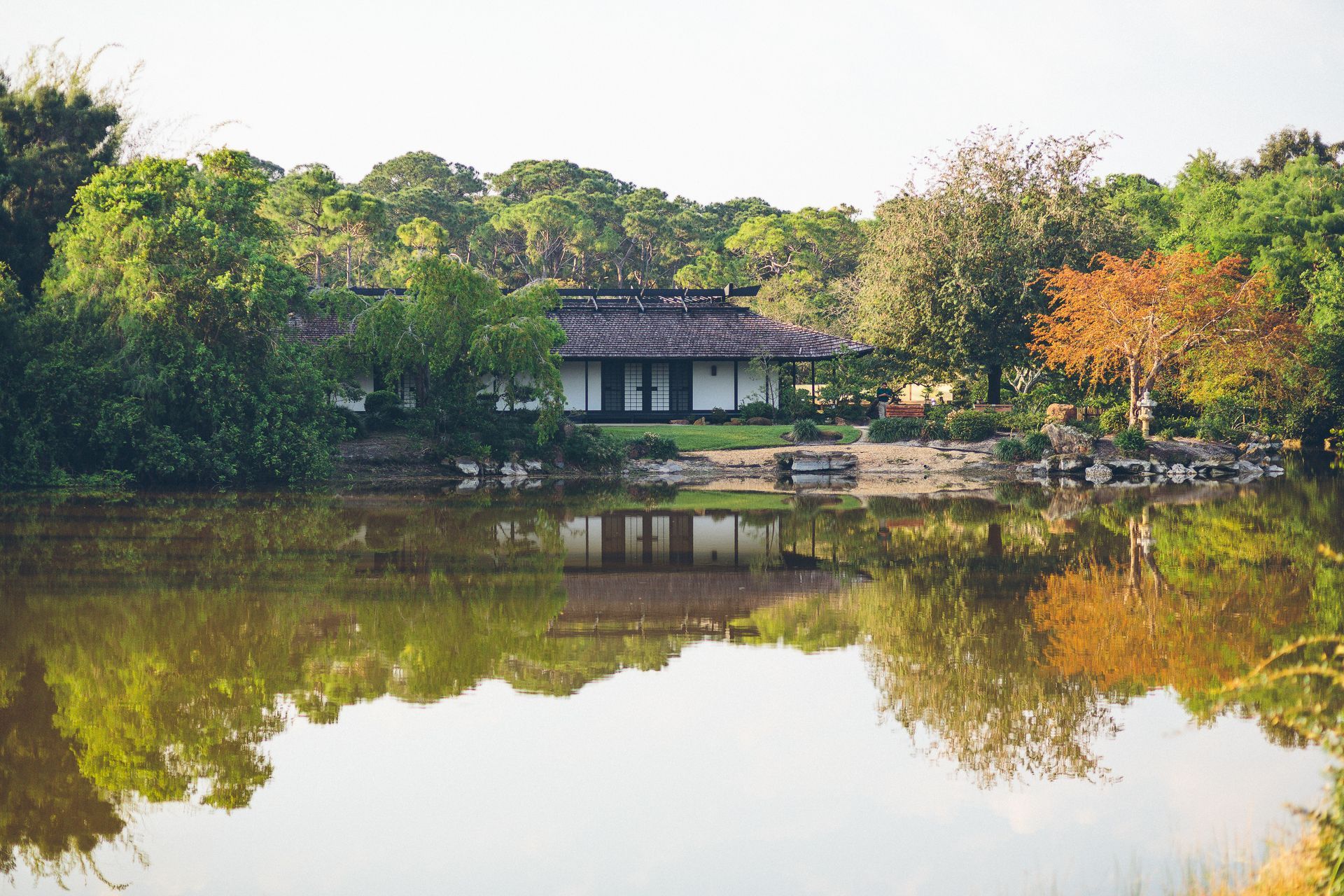 A house is reflected in the water of a lake surrounded by trees.