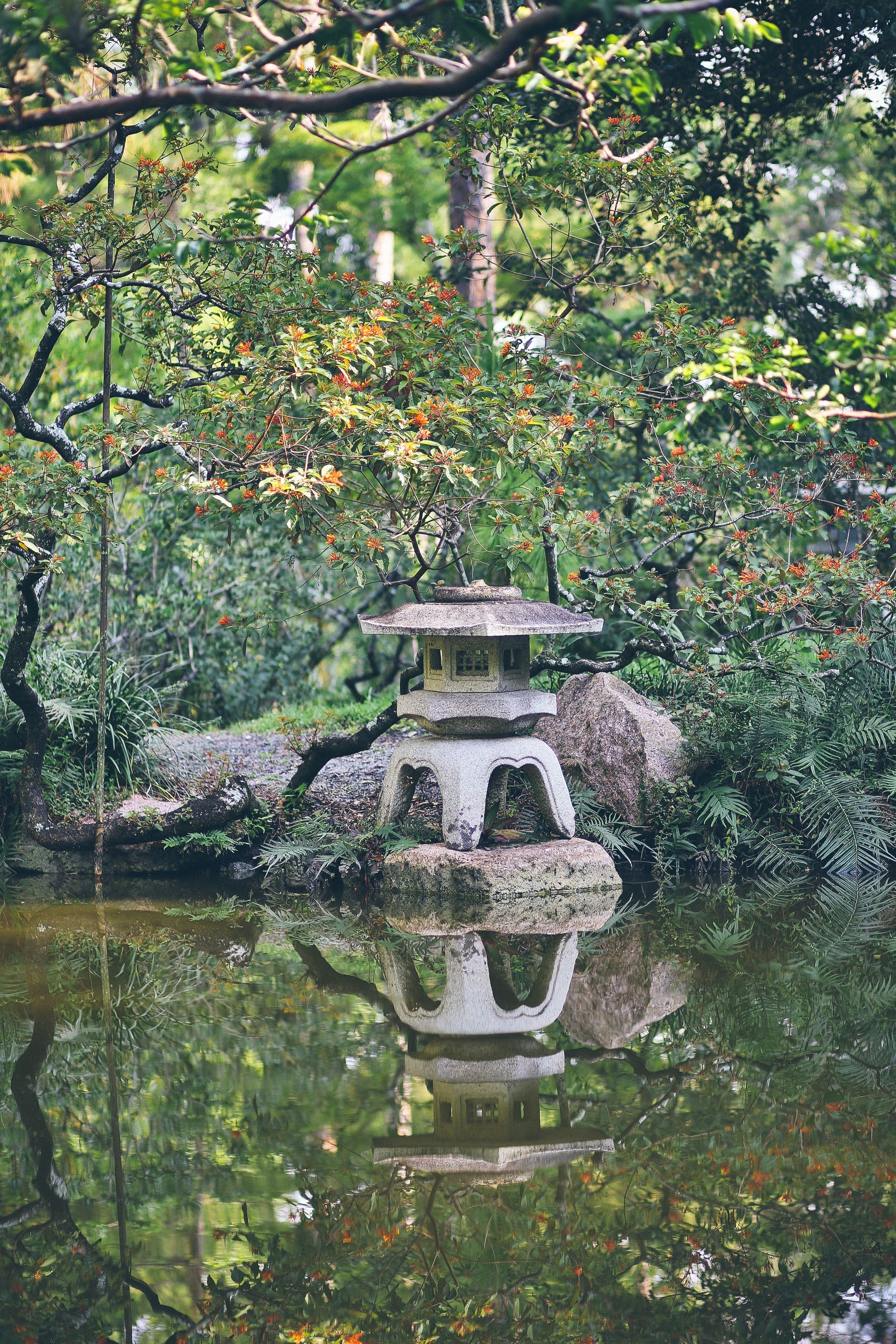 A stone lantern is sitting in the middle of a pond surrounded by trees.