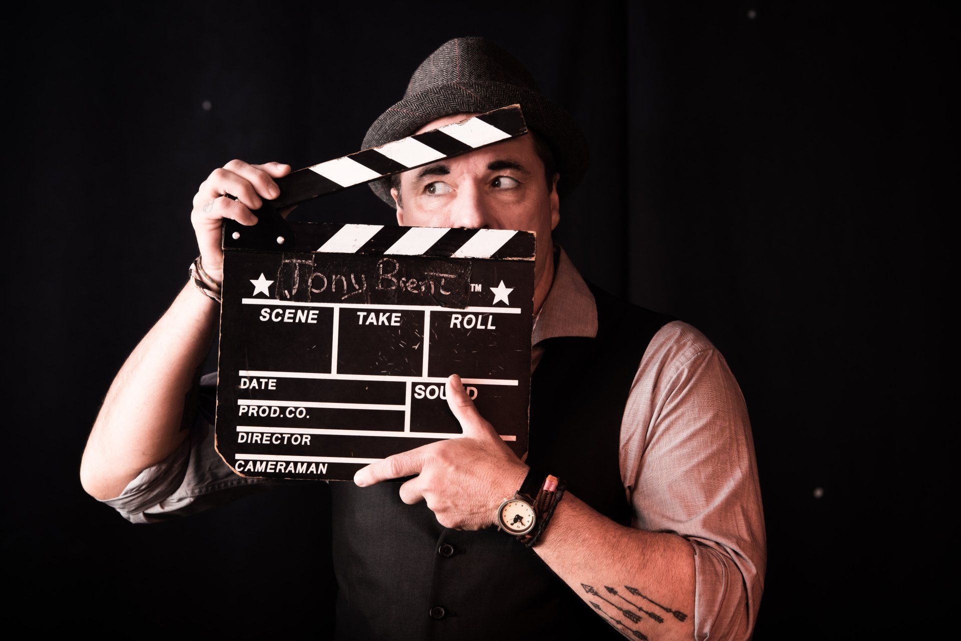 A man in a hat is holding a clapper board in front of his face