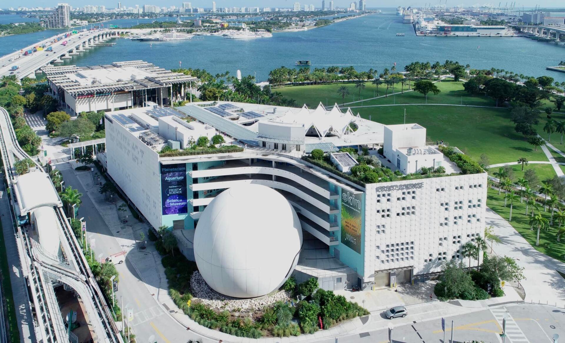 An aerial view of a large white building surrounded by trees and a body of water.