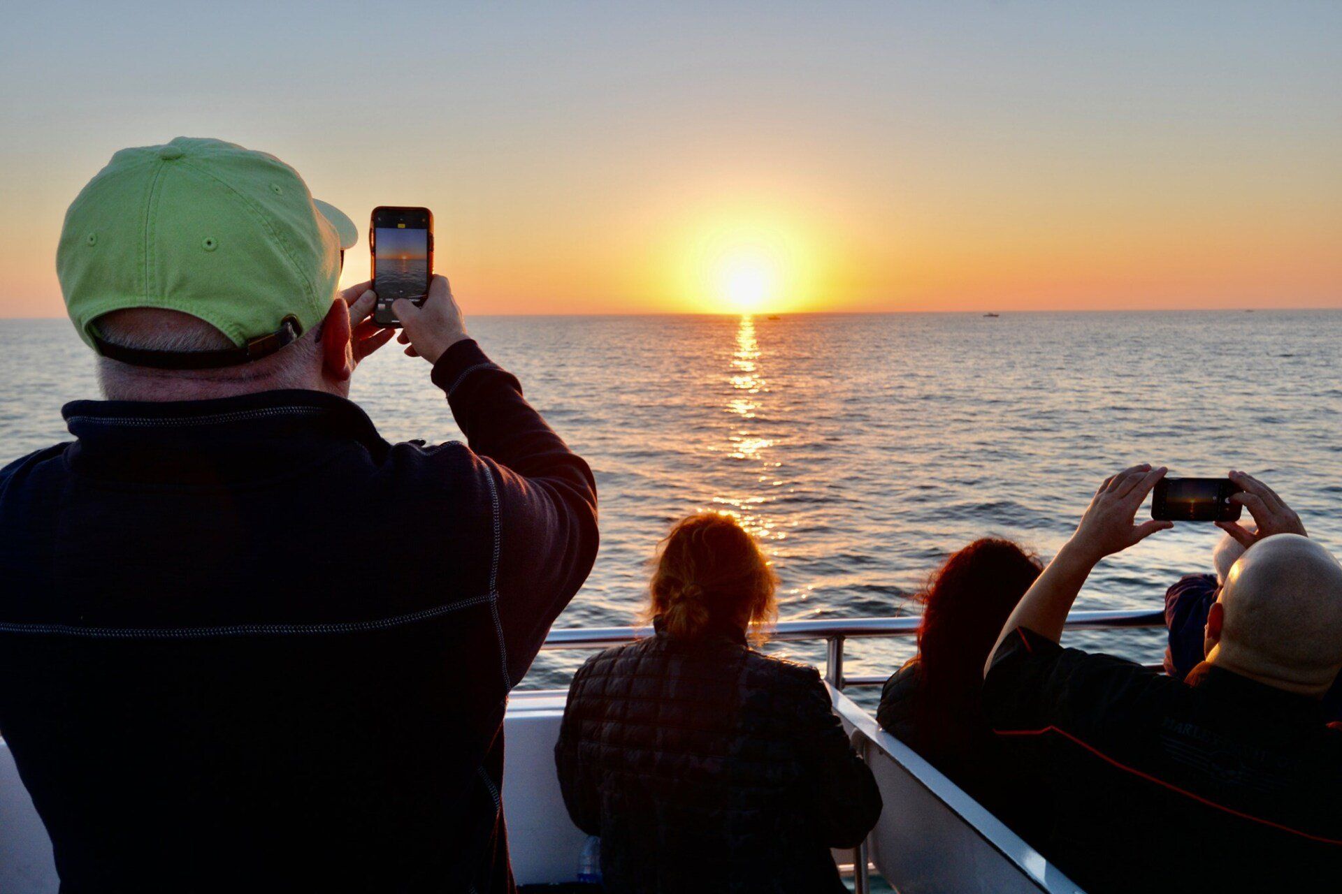 A group of people are taking pictures of the sunset on a boat.