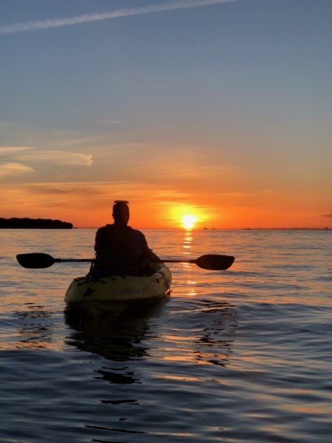 A person is paddling a kayak in the ocean at sunset.