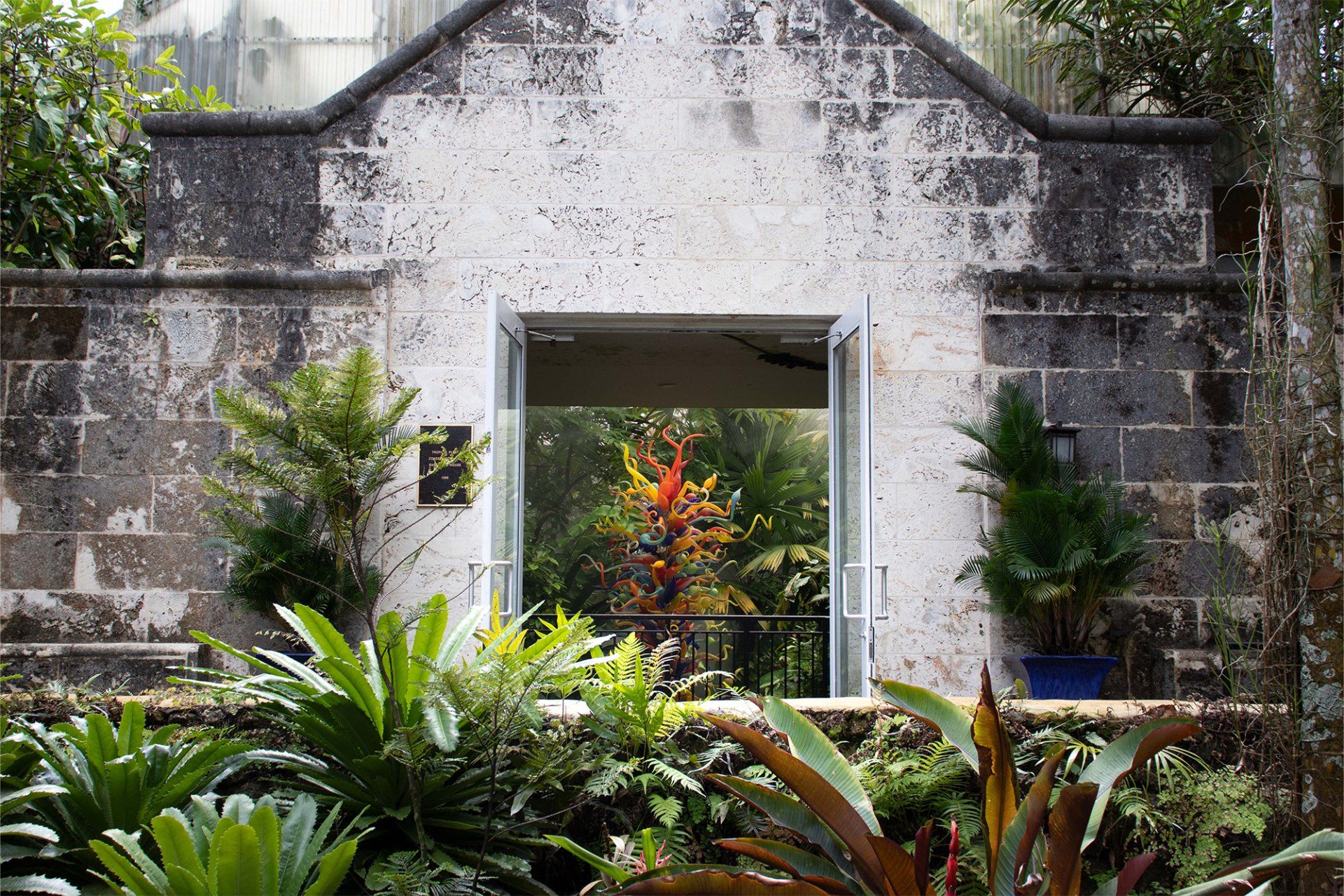 A brick building with a door that is open and surrounded by plants