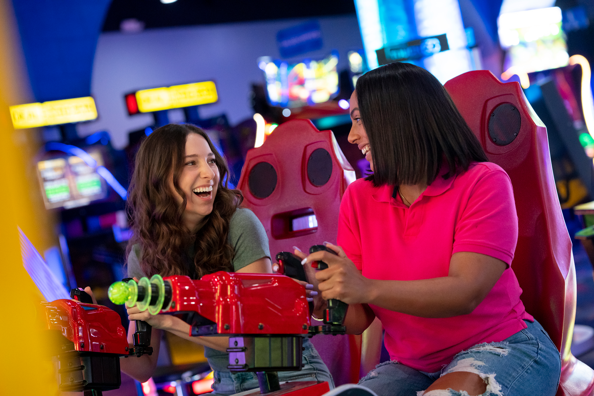 Two women are playing video games in an arcade.