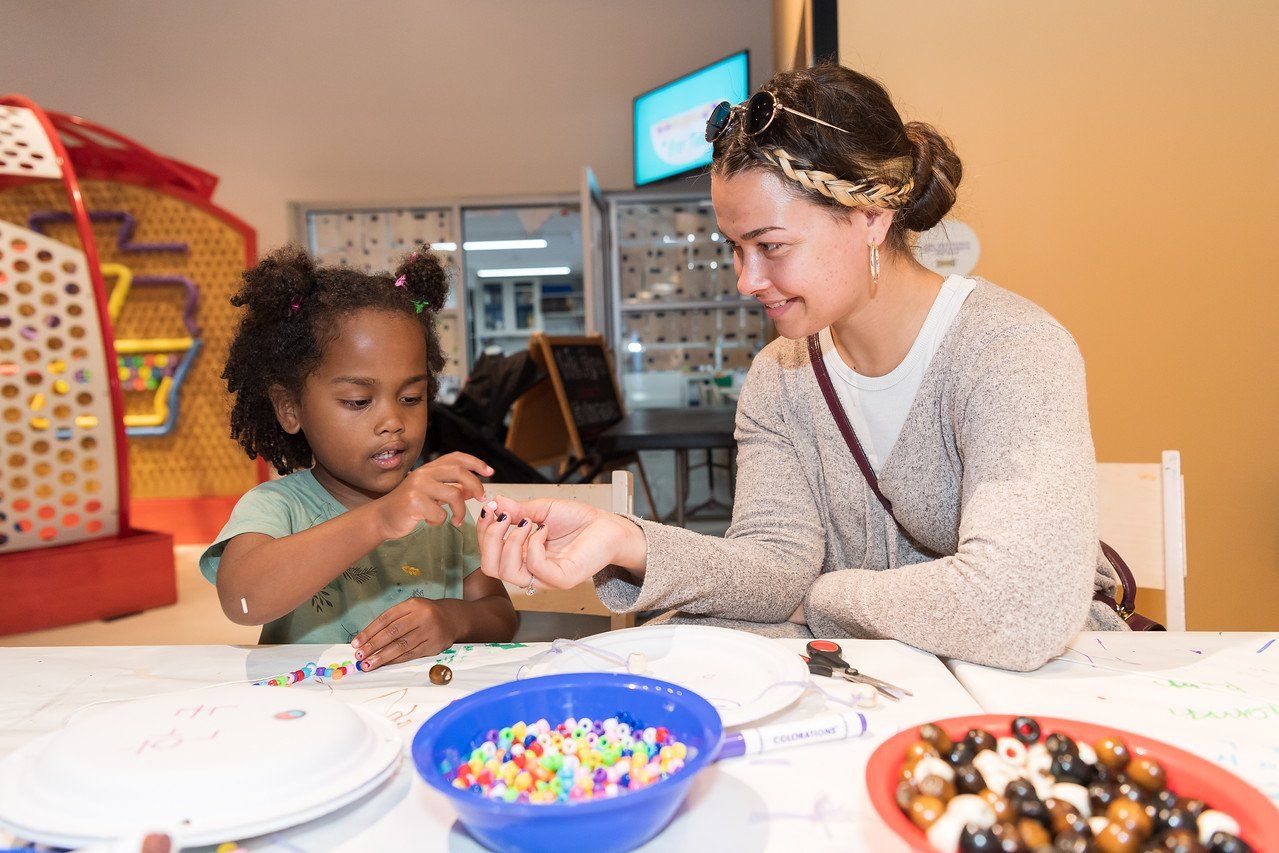 A woman and a little girl are sitting at a table playing with beads.