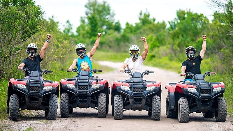 A group of people are riding atvs on a dirt road.