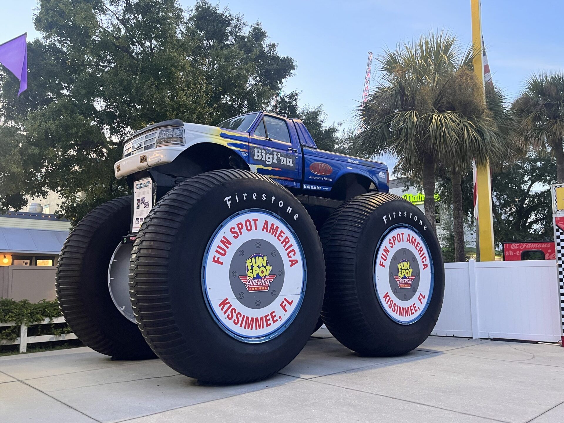 A blue monster truck with giant tires is parked on a sidewalk.