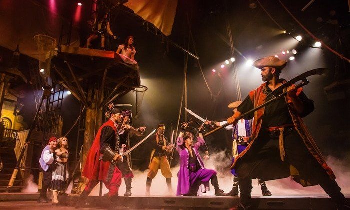 A group of people are standing on a stage holding swords in a pirate show.
