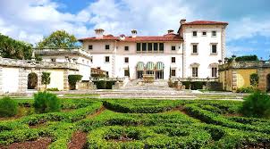 A large white house with a red roof is surrounded by a lush green garden.