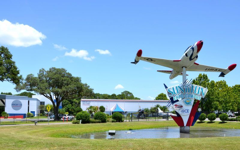 A large airplane is flying over a fountain in front of a building.