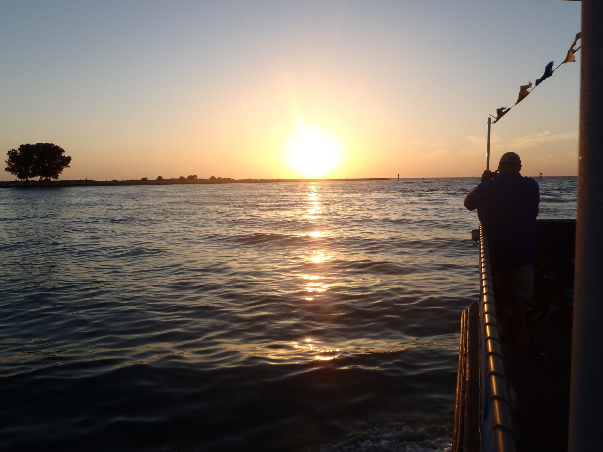 A man stands on a boat watching the sun set over the ocean