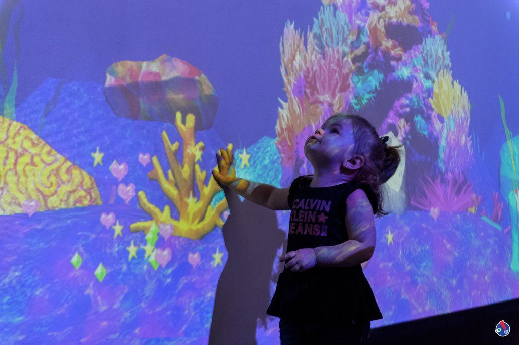 A little girl is standing in front of a projection of a coral reef.