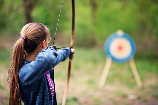 A young girl is aiming a bow at a target.
