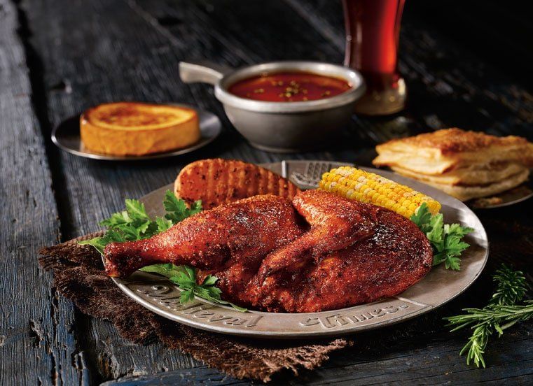 A plate of food with chicken and corn on the cob on a wooden table.