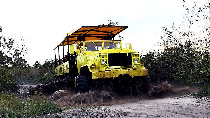A yellow truck is driving down a dirt road.