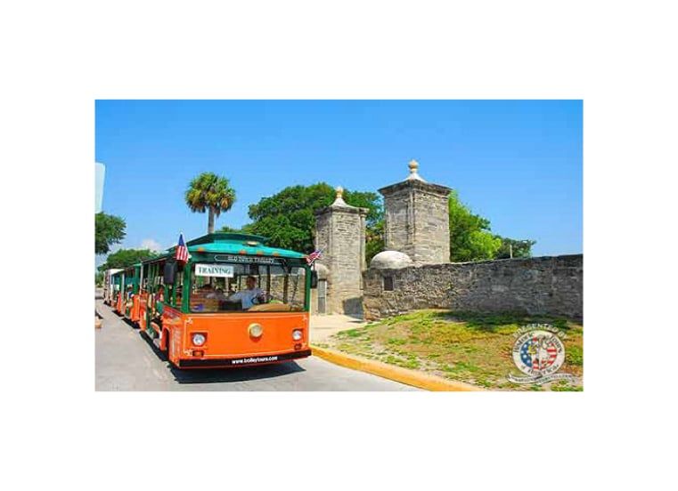 A trolley is driving down a street next to a stone wall.