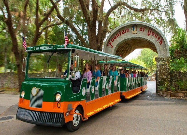 A green and orange train is going through a fountain of youth entrance.