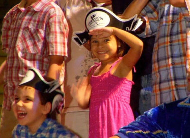 A little girl in a pink dress is wearing a pirate hat