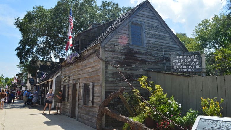 A group of people are walking down a sidewalk in front of a small wooden house.